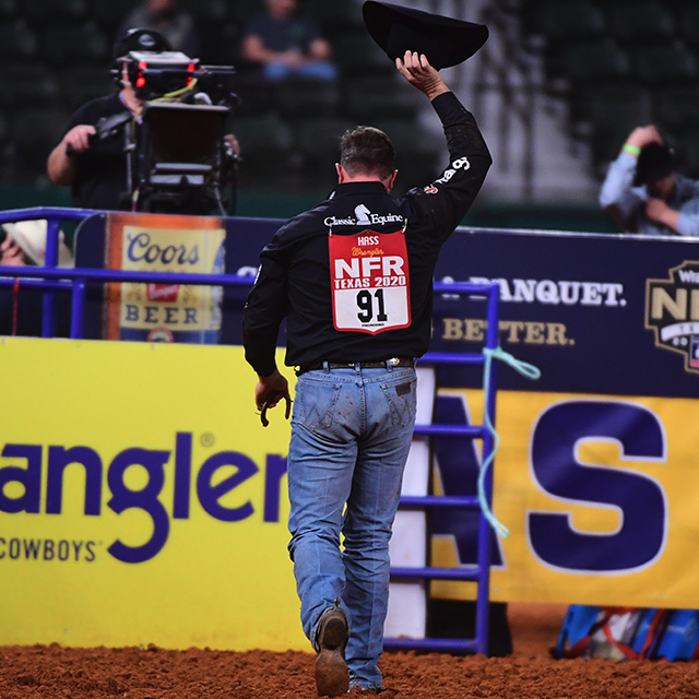 Vaquero alejándose de la cámara con su mano derecha sosteniendo su sombrero de vaquero en el aire en las Finales Nacionales de Rodeo.